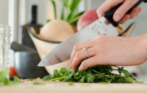 Woman holding a sharp knife, cutting herbs on a chopping board and prepping her veg