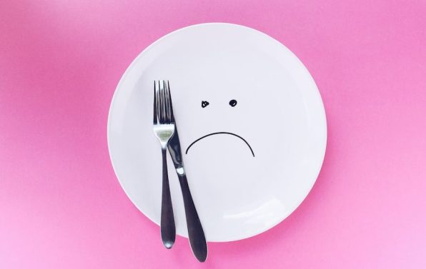 Empty white plate and silver cutlery, on a bright pink background. Frown face drawn on the plate. A guide to intermittent fasting after 40.